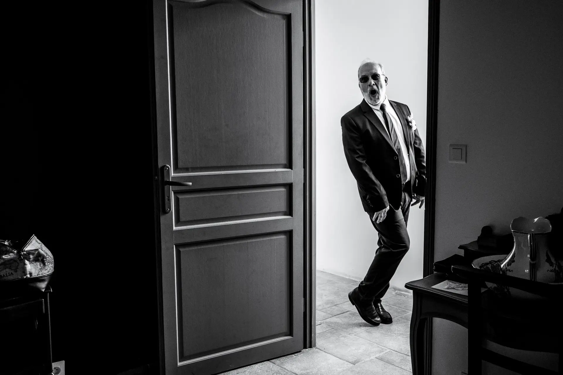 Photo de mariage noir et blanc en Eure-et-Loir : le père de la mariée, portant des lunettes de soleil, exprime une surprise totale et joyeuse en découvrant sa fille pour la première fois dans sa robe