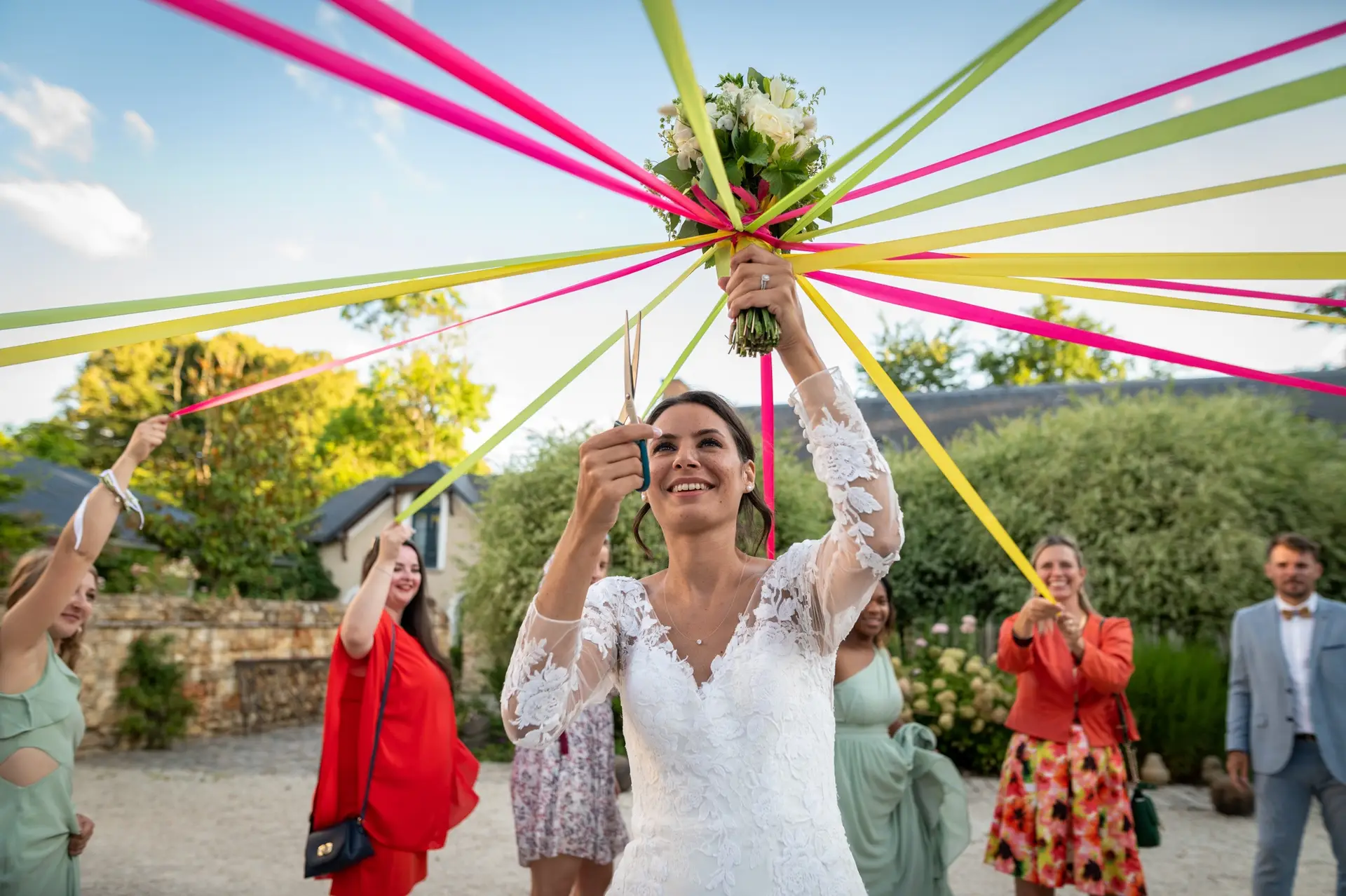 Photographe mariage Domaine de Quincampoix - Mariée entourée de ses amies pour le jeu des rubans du bouquet en extérieur.
