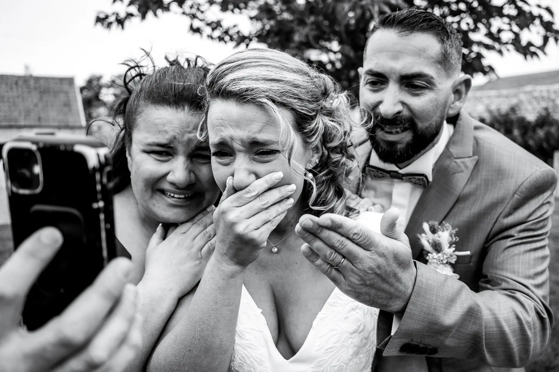 Photo de mariage noir et blanc à la Ferme des Festivités (28) : émotion intense d'une mariée en larmes lors d'un appel en visio, entourée de ses proches.