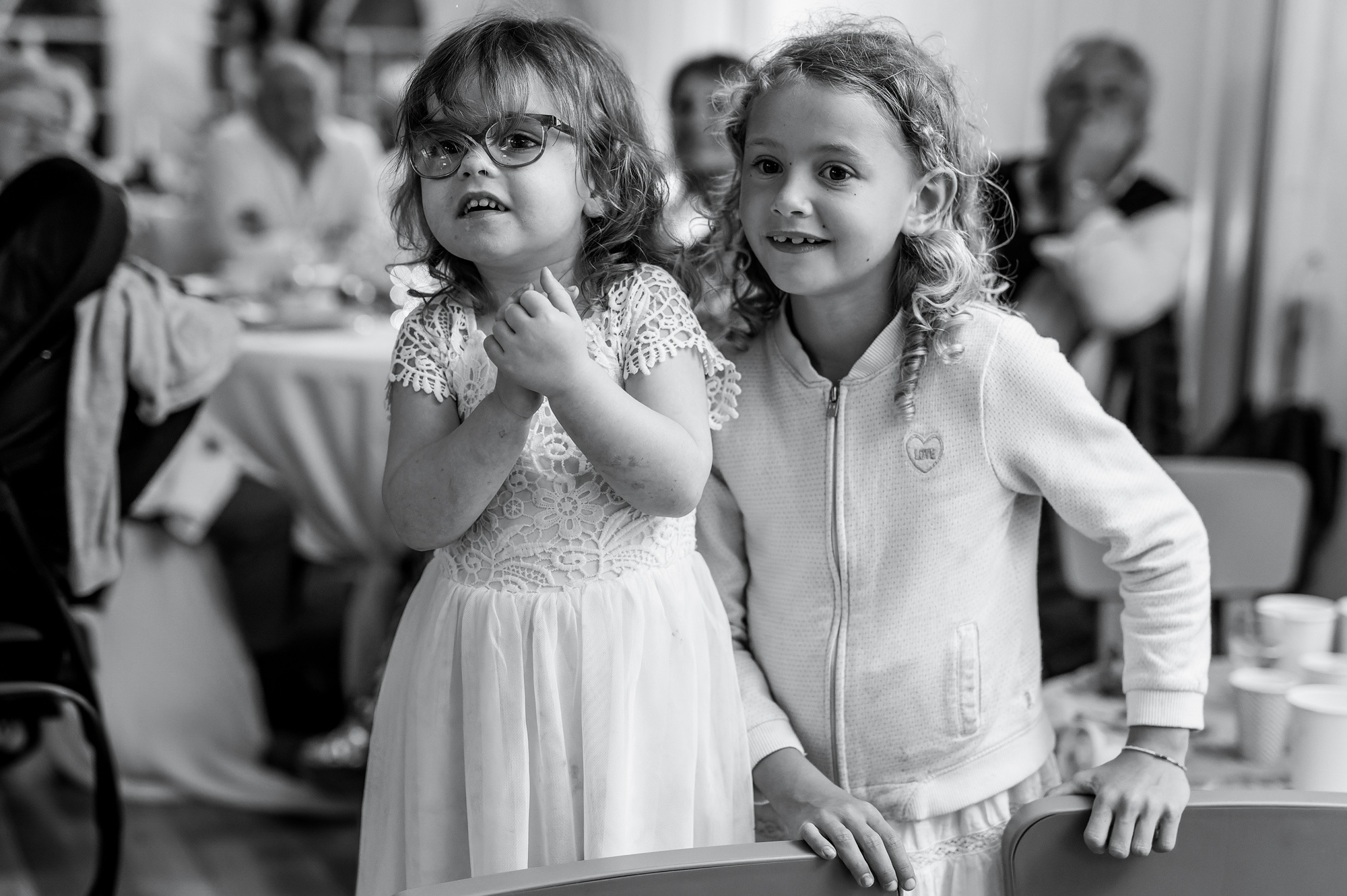 Photographe mariage Pontgoin - Deux jeunes filles attentives et souriantes lors d'une réception de mariage en noir et blanc.