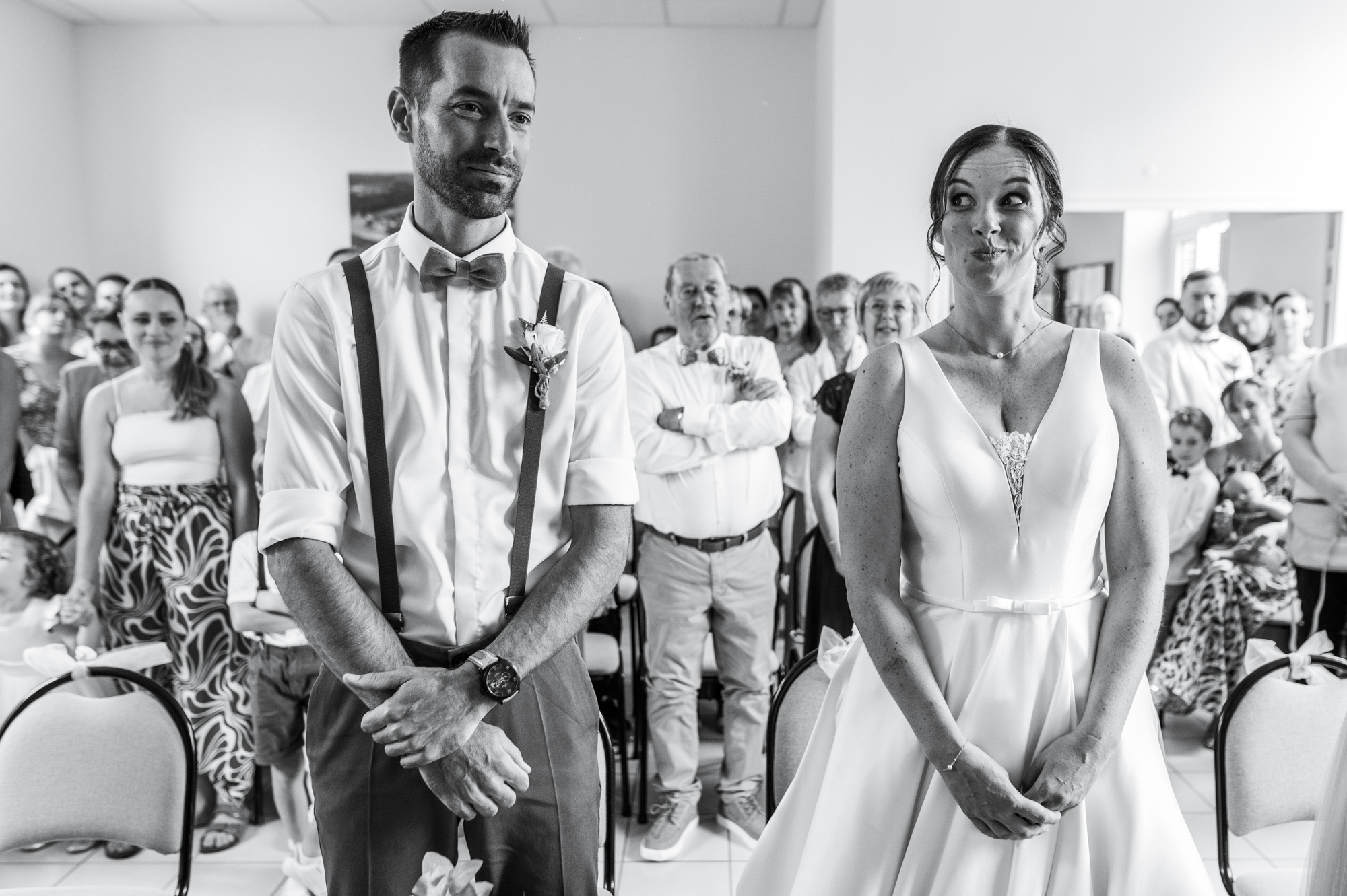 Photographe mariage Saussay - La mariée faisant une grimace complice à son mari pendant la cérémonie en noir et blanc.