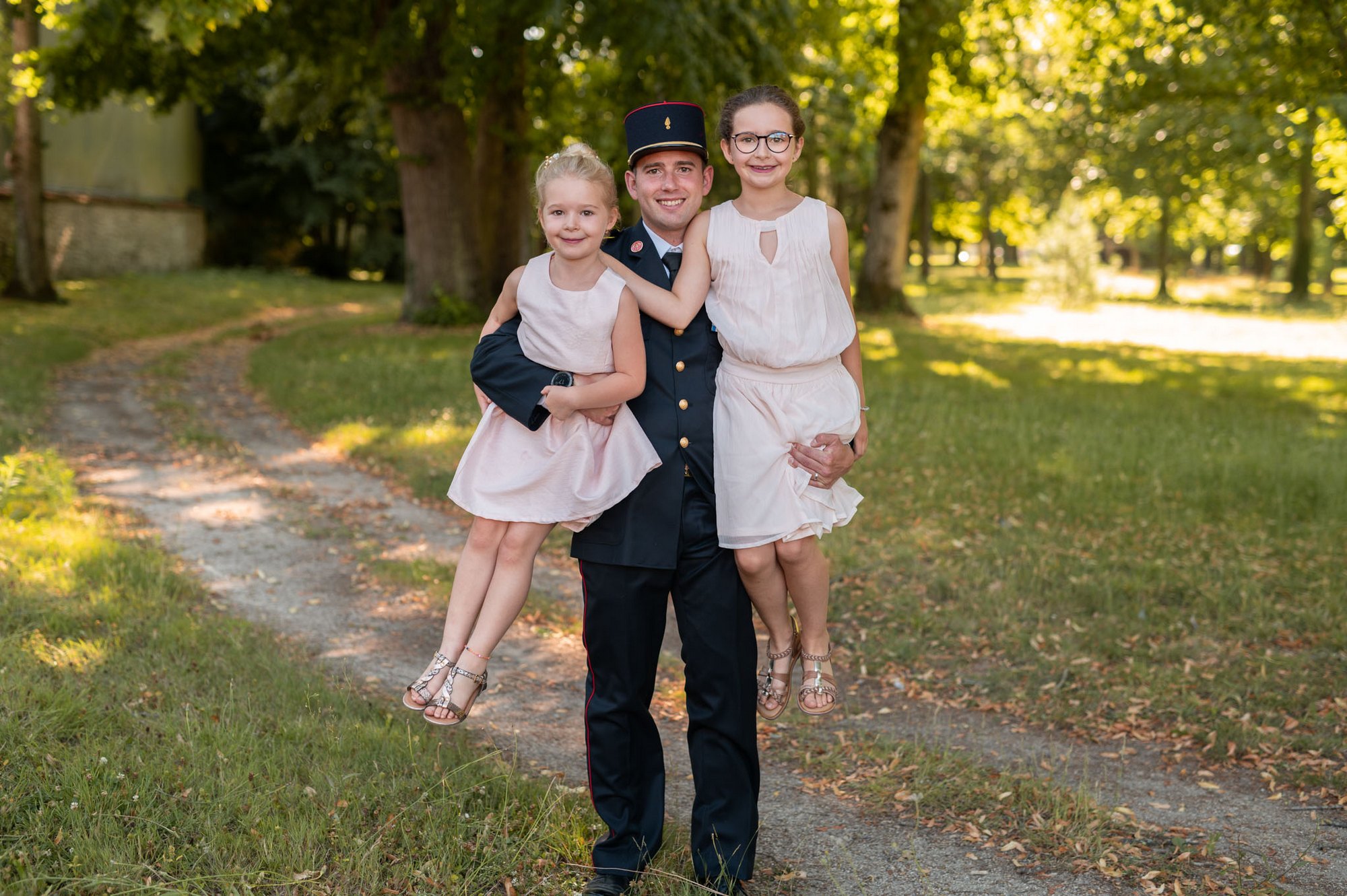 Photographe mariage Yvelines (78) - Le marié en uniforme militaire pose fièrement en portant deux jeunes demoiselles d'honneur dans un parc.