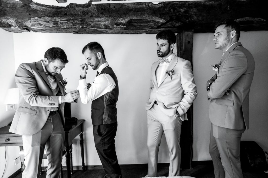 Photographe mariage Eure-et-Loir - Scène de préparatifs du marié entouré de ses témoins en noir et blanc dans un domaine du 28.